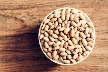 Beans (Phaseolus) in white porcelain bowl on wooden background, vegetarian concept.