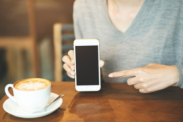woman hand holding mobile smart phone with blank desktop screen and finger touching while drinking coffee in cafe shop. 