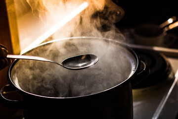 the man stirs the soup in the pan from which steam comes