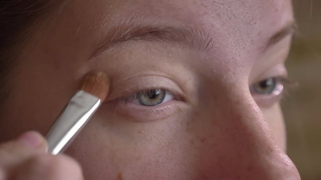 Closeup portrait of young caucasian make-up artist applying concealer to her eyelid with a brush