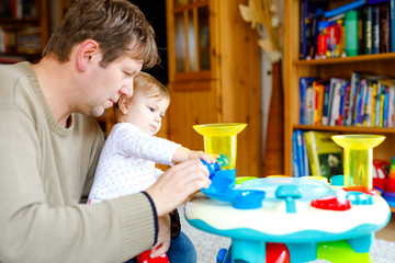 Obraz premium Happy proud young father having fun with baby daughter, family portrait together. Dad playing with baby girl with educational sorter toy with different colorful balls. Man with little child at home.