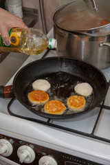 fried syrniki on a black round skillet. Sunflower oil is poured into the pan