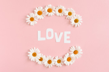Word Love laid out of letters cutting out of paper. Chamomile flowers 