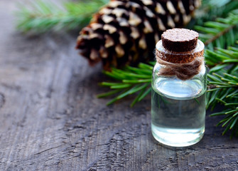 Spruce essential oil in a glass bottle and green fir tree branches with cones on old wooden table.Fir needle aroma oil for spa,aromatherapy and bodycare.Selective focus.