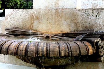 Parte de una fuente ornamental de agua en piedra con una paloma torcaz bebiendo y descansando en...