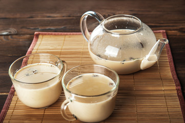 Masala tea on a textural wooden background. A teapot is a transparent tea pot with mugs and Indian national tea masala. Milk, ginger, cardamom, cloves, nutmeg, star anise, cinnamon