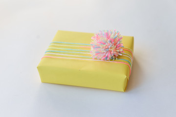 Obraz na płótnie Canvas yellow gift box on a white background. winter holidays, pompom from threads, warm. unusual