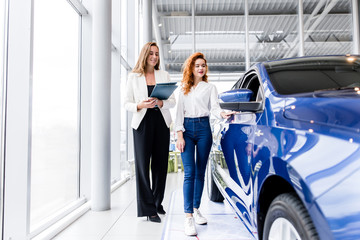 Two girls go to the showroom choosing a new car to buy