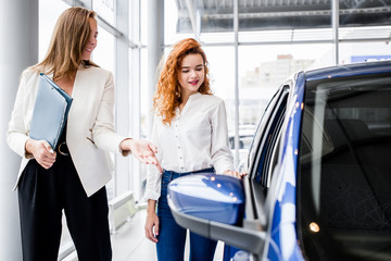 Girl shop consultant showing a new car to the buyer