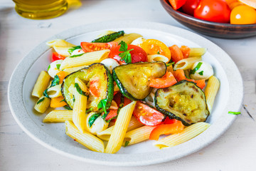 Margarita pasta in a plate on a wooden table - penne with tomatoes, zucchini, mozzarella and basil