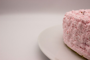 The piece of a cream pink cake on a plate on a white-gray background. Image with a copy space area.