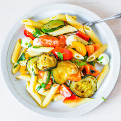 Margarita pasta on a plate top view - penne with tomatoes, zucchini, mozzarella and basil.