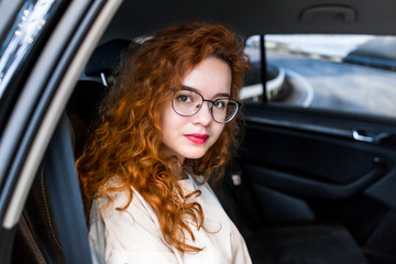 Young beautiful red-haired girl sitting in the back seat in the car
