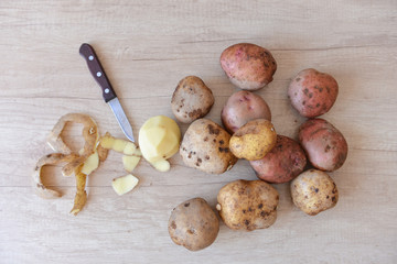 raw potatoes in the process of cleaning lies on a wooden table next to a small knife. cleaning, peel. clean potatoes