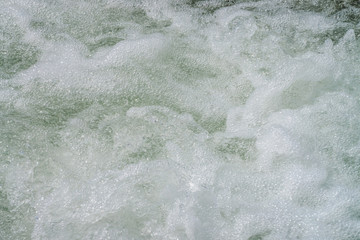 Natural texture of foamed water surface. Rapids of river close-up. Fast flow in mountain creek. Background of clean water waves with copy space. Textured foam of shiny stream. Fast river texture.