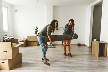 Lesbian couple carrying carpet in new home 