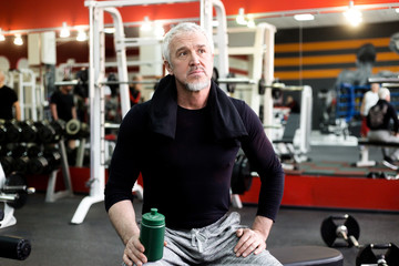 Adult gray-haired man holding a bottle of water resting after exercise
