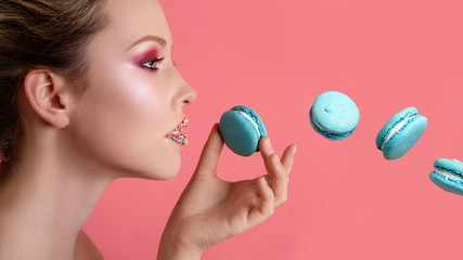 Beauty fashion model girl with colourful makeup taking blue macaron. Beautiful woman, bright make-up. Diet,dieting concept. Sweets.