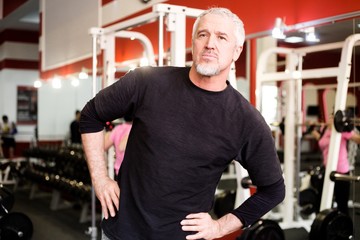 Adult gray-haired man does warm up in the gym