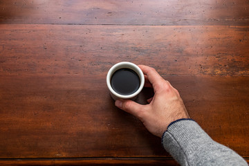 Male hand holding a cup of coffee on a wooden table. Overhead view.
