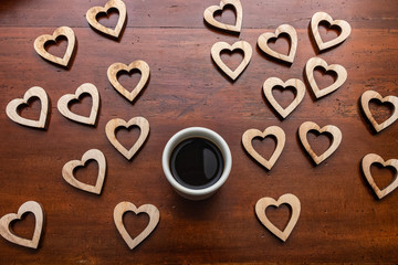 Above view of coffee cup on wooden table surrounded by wooden heart shapes
