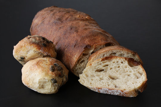 Just baked homemade loaf with bread slices and buns with seeds - rustic quality with sourdough. Beautiful picturesque close up image with stacked focus on black background.