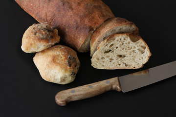 Just baked sourdough homemade bread and buns with seeds - rustic quality with knife lying by slices of bread. Beautiful picturesque image on black background.