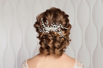 Wedding female hairstyle low beam on the head of a brown-haired girl back view on a light...