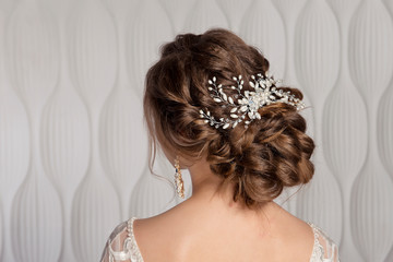 Wedding female hairstyle low beam on the head of a brown-haired girl back view on a light background. - obrazy, fototapety, plakaty