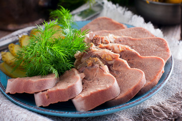 Chopped boiled beef tongue on a plate with fresh herbs and pickled cucumbers, horizontal