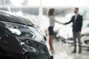 Car dealer and client shaking hands in showroom.