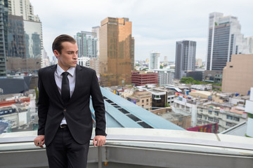 Young businessman thinking outdoors in city with rooftop view