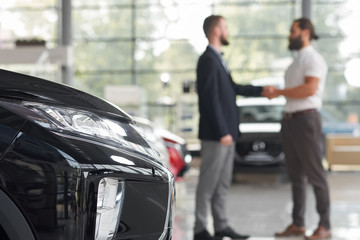 Car dealer shaking hands with client in car showroom.