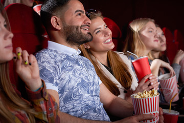 Brunette Arabian man and blonde smiling woman in cinema.