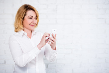 portrait of cheerful mature business woman using smart phone over white wall