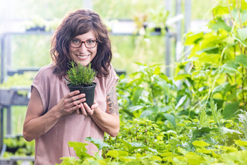 Fröhlich lächelnde Frau in einer Gärtnerei mit einem Topf Olivenkraut
