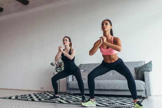 Two fit women exercising together doing squats at home