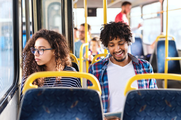 Two young persons sitting next to each other in city bus. Girl looking through window while guy having earphones on ears and using tablet. © Dusan Petkovic