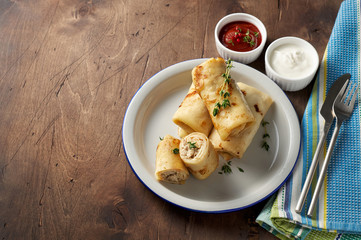 Savory crepe rolls with ground meat filling served with sour cream and tomato sauce