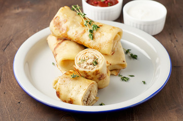 Savory crepe rolls with ground meat filling served with sour cream and tomato sauce