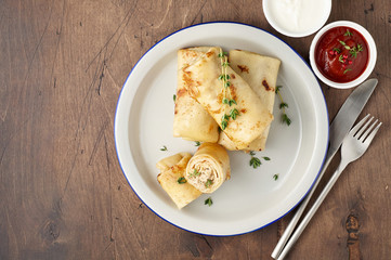 Savory crepe rolls with ground meat filling served with sour cream and tomato sauce