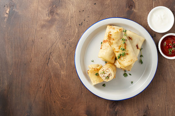 Savory crepe rolls with ground meat filling served with sour cream and tomato sauce