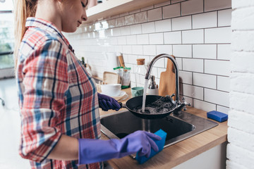 Young woman wearing rubber gloves washing frying pan in kitchen
