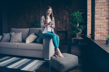 Obraz premium Full length body size photo portrait of cheerful positive concentrated cute nice glad slim fit she her girl student sitting on divan pouffes using telephone smartphone