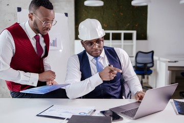 African businessman Builder in a white helmet shows the execution plan of a work colleague on the...