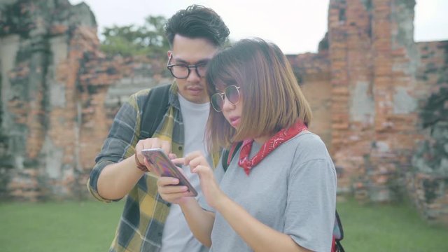 Traveler Asian couple using smartphone for direction and looking on location map while spending holiday trip at Ayutthaya, Thailand, backpacker sweet couple enjoy journey in traditional city.