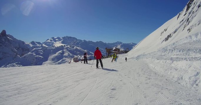 skiers on sunny ski track in alpine mountains