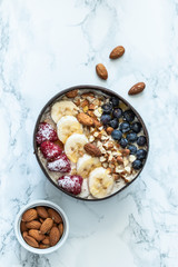 Healthy breakfast berry smoothie bowl topped with blueberry,almond, banana, granola and raspberries. Top view. white marble background.
