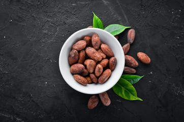 Cocoa beans in a bowl on a black background. Top view. Free copy space.