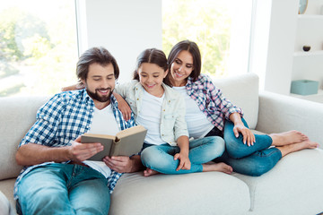 Portrait of nice cute lovely trendy attractive cheerful cheery people mom dad sitting on divan reading free time in light white modern interior indoors